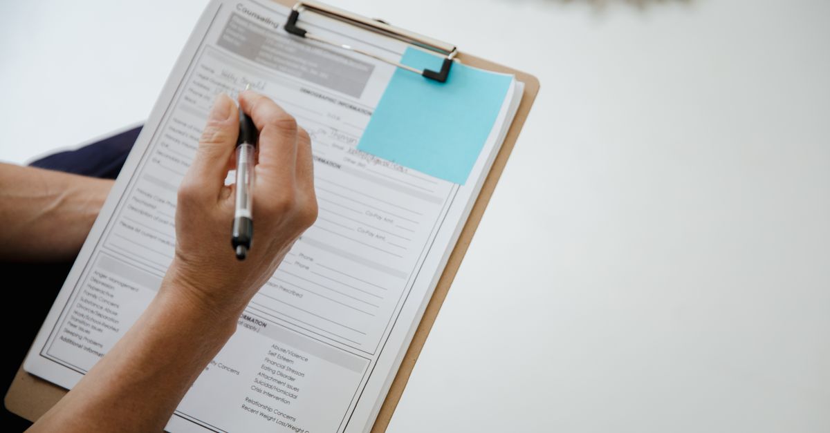 Une main remplit un formulaire papier sur une planchette à pince