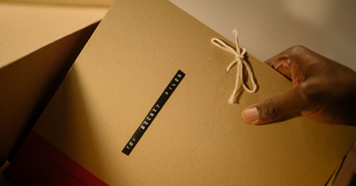 Une main sort un dossier de documents d'une boîte d'archives
